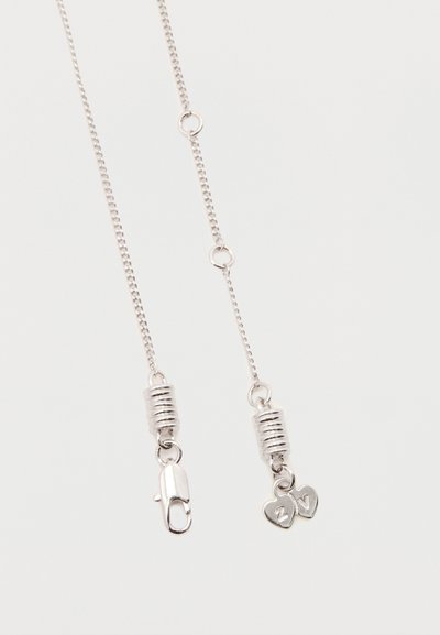 Divas sudraba ķēdes ar atsperes aizdares; viena ķēde beidzas ar aizdari, bet otra ar diviem maziem sirdīšu formas piekariņiem, uz kuriem ir iegravēti burti "Z" un "V".