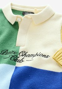 Polotshirt i stickad tyg med gröna, krämfärgade, ljusblå och blå sektioner. Svart text "Paris Champions Club" på den krämfärgade delen.