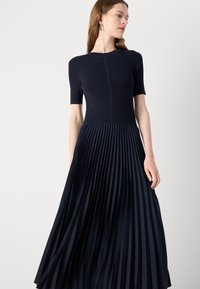 Navy dress with a fitted knit bodice and pleated skirt. Short sleeves, textured upper, flowing fabric, and smooth pleats.