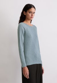 Garais piedurkņu tops mīkstā, gaiši zils audums ar smalku tekstūru. Iespējo apaļa kakla izgriezums un brīva piegriezuma, kombinēts ar melnajām biksēm.