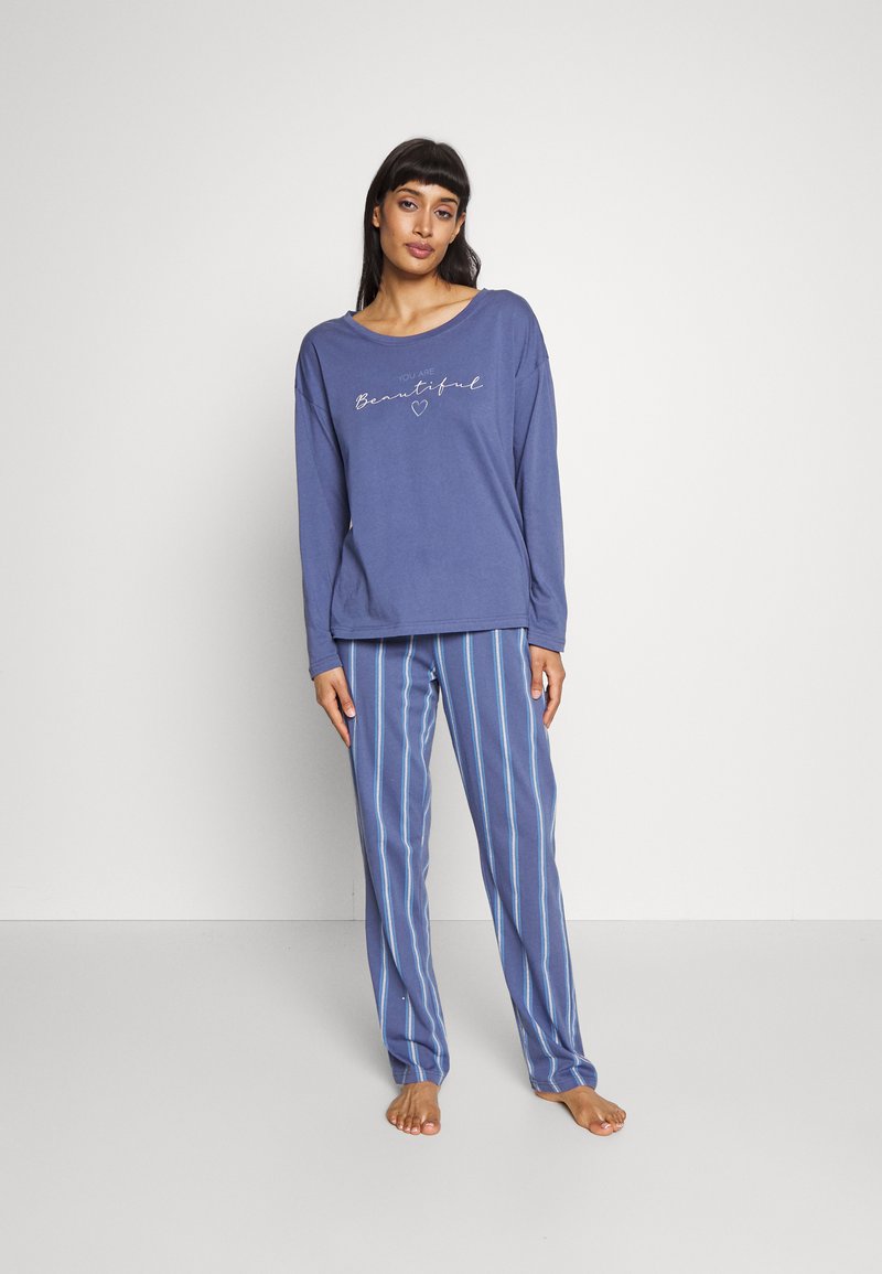Langärmliges, blaues Pyjamaoberteil mit dem Text "Du bist schön", kombiniert mit blauen gestreiften Hosen. Weicher Stoff; legerer Schnitt und lässiger Stil.