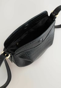 Sac à main en simili cuir noir avec une texture crocodile, un haut ouvert et un accent en métal doré sur la sangle. Intérieur spacieux.