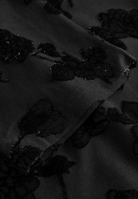 Tissu noir avec des motifs floraux en velours texturé et un subtil scintillement sur un matériau lisse et plié.