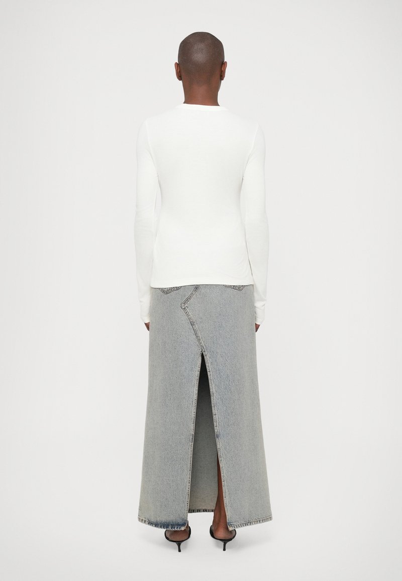 Long-sleeve white top paired with a high-waisted, floor-length denim skirt featuring a front slit and contrasting stitching details.