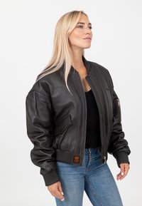 Czarna skórzana kurtka bombowca z prążkowanymi mankietami i dołem, zamkiem błyskawicznym z przodu oraz bocznymi kieszeniami. Posiada naszywkę z logo na lewym ramieniu.