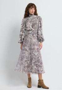 Blomsterprydet, semi-gennemsigtig kjole i bløde lavendel- og beige nuancer, med høj halsudskæring, elastisk talje og lange puffede ærmer.