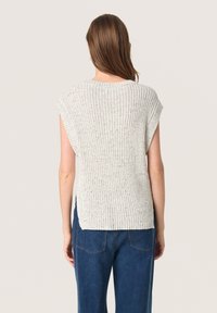 Top rivestito a coste di colore grigio chiaro con maniche corte, caratterizzato da una scollatura ampia e fessure laterali. Abbinato a pantaloni di denim blu scuro.