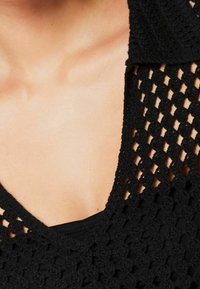 Czarny szydełkowany top z dekoltem w szpic, ażurową strukturą i krótkimi rękawami, odsłaniający jednolitą, czarną warstwę pod spodem.