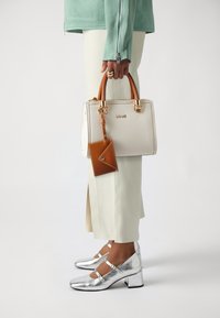 Borsa bianca con dettagli marroni, hardware dorato e un portacarte abbinato. Indossata con pantaloni crema e scarpe con tacco argento lucido.