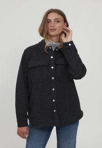 Tmavo šedá košľa-jacket z vlnenej zmesi s dvoma náprsníkmi, zapínaním na gombíky a zaobleným lemom. Obsahuje golier a zjavné detaily prešívania.