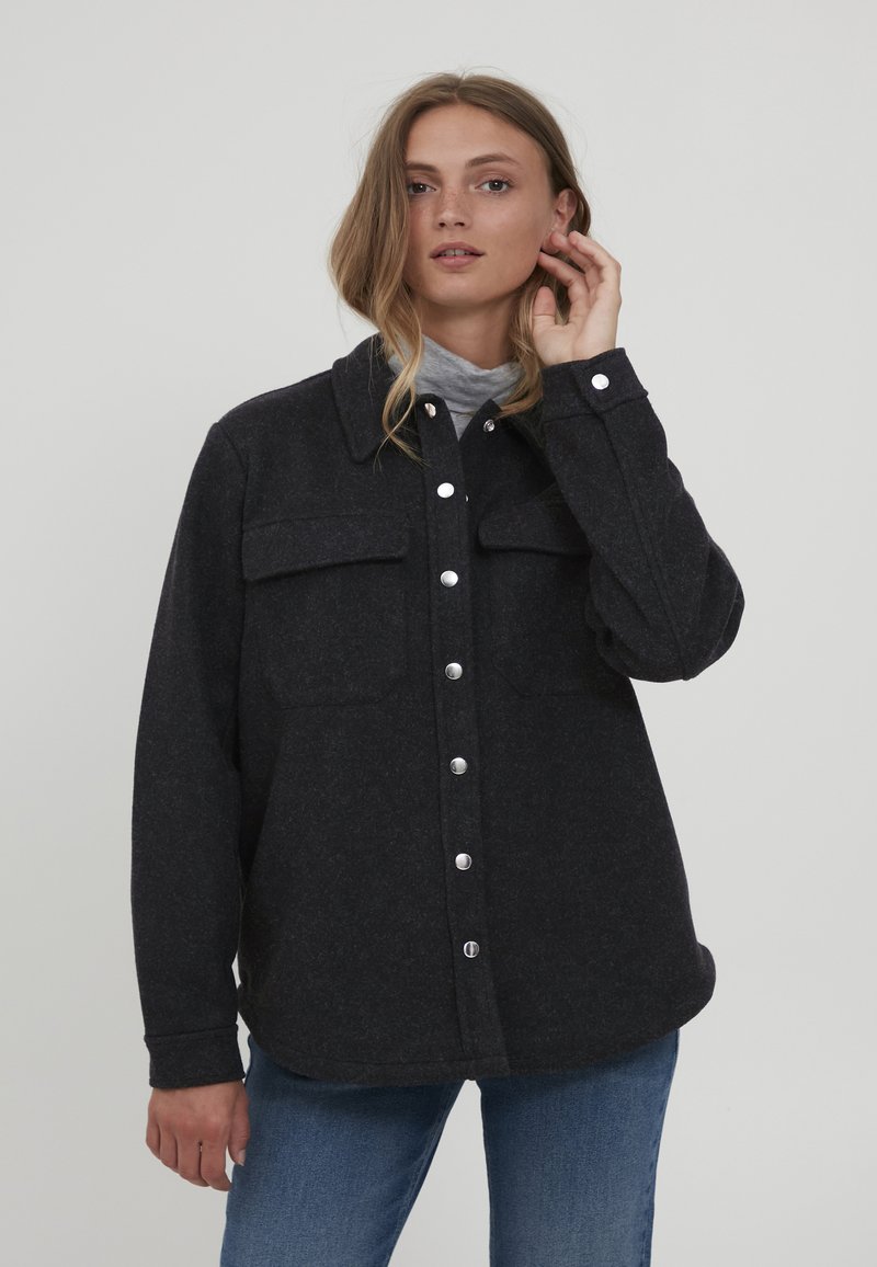 Tmavo šedá košľa-jacket z vlnenej zmesi s dvoma náprsníkmi, zapínaním na gombíky a zaobleným lemom. Obsahuje golier a zjavné detaily prešívania.