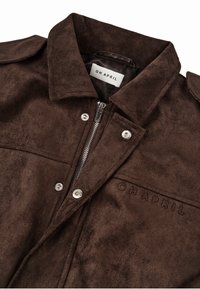 Rudos veliūro striukės su apykakle, sidabriniu užtrauktuku ir spaudėmis. Yra iškeltasis logotipas ir sklandus paviršius.