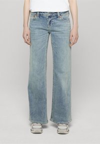 Modré džínové kalhoty širokých nohavic s vybledlým efektem, pěti kapsami, šicím zdobením a volným střihem. Kombinované s světle zbarvenými teniskami.