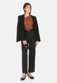 Top marrone drappeggiato, blazer nero su misura, jeans neri a vita alta, scarpe nere con tacco e una piccola borsa nera con dettagli dorati.