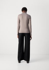 Haut à manches longues de couleur gris clair au design ajusté ; associé à un pantalon noir à jambes larges avec de petites accents métalliques.