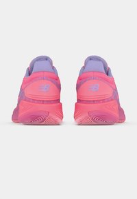Ett par rosa och lila New Balance träningsskor visas bakifrån, vilket framhäver varumärkesloggan och den texturerade sålen.