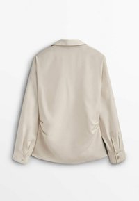 Chemise beige à manches longues avec poignets boutonnés, tissu doux et col classique, vue de dos sur fond blanc.
