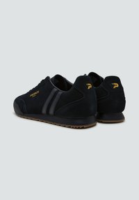 Sneaker in suede nera con due strisce nere, suola in gomma testurizzata e dettagli in oro con il nome del marchio "PATRICK" visibile.