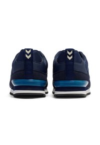 Marinblå träningsskor med en texturerad ovandel, med en blå accent på sulan och tre vita chevrondetaljer på hälen.