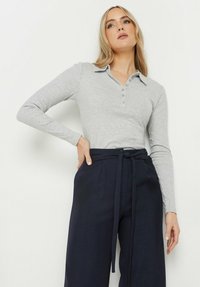 Szary długi rękaw polo z kołnierzykiem i guzikami, zestawiony z spodniami o wysokim stanie w kolorze granatowym, z zawiązywanym pasem.