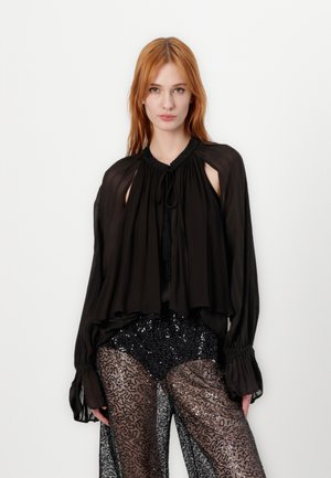 Zwarte chiffon blouse met lange mouwen, ronde halslijn en uitsnijdingen. Heeft een met kralen versierde kraag en een zachte val. Sprankelende zwarte broek eronder.