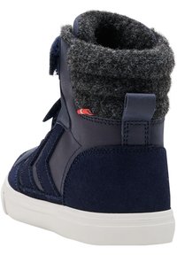 Sneaker alta blu navy con battistrada in suede e polsino in lana, caratterizzata da una suola bianca, materiale testurizzato e un piccolo dettaglio rosso accentato.