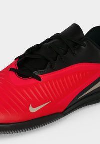 Κόκκινο και μαύρο αθλητικό παπούτσι Nike με μαύρα κορδόνια και λευκό λογότυπο Nike στο πλάι, εμφανίζεται από κοντινή πλευρική γωνία.