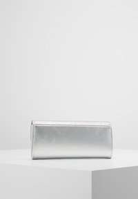 Pochette métallique argentée avec une texture lisse et un bord supérieur scintillant. Forme rectangulaire, design minimaliste, avec une fermeture éclair.