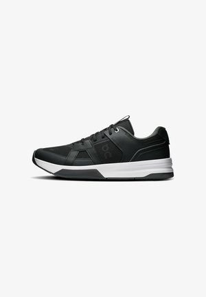 Chaussure de sport basse noire et grise avec semelle blanche, dessus en mesh et cuir, fermeture à lacets et col rembourré sur fond blanc.