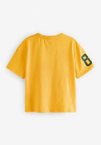 Gele katoenen T-shirt met korte mouwen, met een groene "8" bedrukt op de rechtermouw. Eenvoudig ontwerp met een ronde hals.