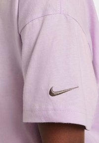 Manga de camiseta de algodón color púrpura claro con un logo de Nike bordado en el puño. Los detalles de las costuras son visibles en el hombro.