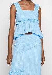 Ljust blå randig croppad topp med volangspännen och utsvängd nederkant, matchad med en passande åtsittande kjol med volangdetalj i nederkant.