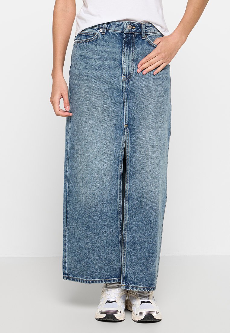 Gonna maxi in denim azzurro chiaro con spacco frontale, design a vita alta, cinque tasche e passanti per cintura. Abbinata a sneaker bianche.