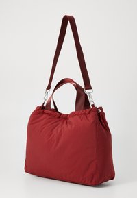 Borsa a tracolla in tessuto rosso con parte superiore arricciata, doppi manici e tracolla staccabile. Texture liscia e forma rettangolare semplice.