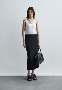 White ribbed tank top, black knee-length skirt with a side zipper, black structured handbag, and black strappy sandals. Simple and modern design.