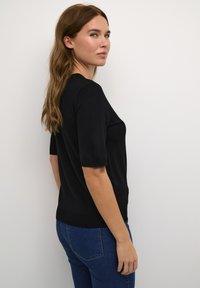 Fekete, rövid ujjú felső kerek nyakkivágással, slim fit szabással és puha tapintással. Kék farmernadrággal párosítva, oldalról nézve.