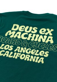 Green cotton t-shirt featuring large yellow text: "Deus ex Machina," "Board & Cycles," "Los Angeles," and "California," with varying fonts.