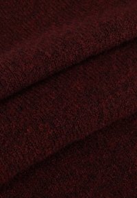 Burgundy tekstureret stof med en blød, fuzzy overflade, der har et subtilt mønster og folder. Materialet fremstår varmt og strikket.