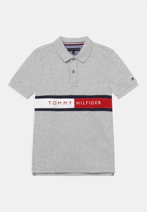 Polo gris clair à manches courtes avec col, deux boutons et une bande horizontale bleu marine, blanche et rouge avec le texte "Tommy Hilfiger" sur la poitrine.