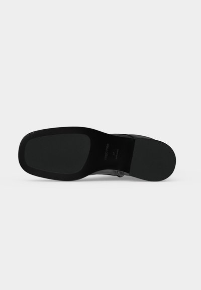Semelle d'une chaussure noire avec une forme d'orteil carrée, montrant une semelle extérieure lisse et un talon bloc sur fond blanc.