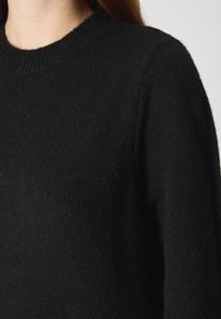 Melna adīta džemperis ar apaļu kakla izgriezumu un garām piedurknēm, ar mīkstu tekstūru un vidēju biezumu. Nav redzamu rakstu vai akcentu.