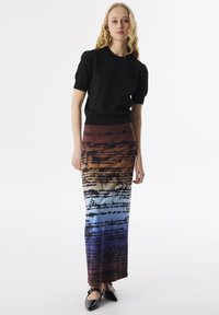 Schwarzes kurzärmliges Oberteil, kombiniert mit einem langen, mehrfarbigen Rock, der ein Verlaufsdesign in den Farben Orange, Blau und schwarzen Textdetails aufweist.