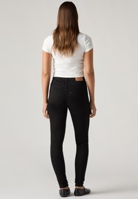 Black skinny jeans with a mid-rise waist, featuring a smooth texture and minimal stitching. Worn with a fitted white t-shirt and black flats.