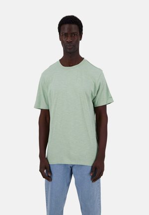 Hellgrünes Baumwoll-T-Shirt mit Rundhalsausschnitt und kurzen Ärmeln, kombiniert mit hellblauen Jeans. Einfaches Design, weiche Textur, lässige Passform.