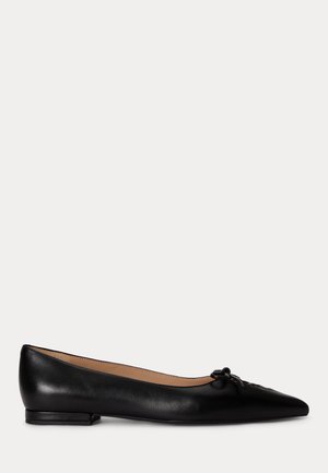 Zapato plano de piel negra con punta estrecha y pequeño detalle de lazo en la parte superior, tacón bajo y forro interior beige.