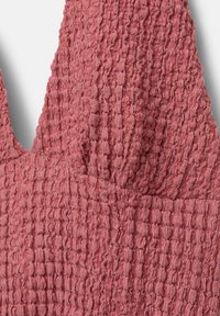 Teksturirani, mekani materijal u boji prašnjavog ružičastog s crinkled površinom. Ima dekolte u obliku slova V i minimalistički dizajn bez vidljivih metalnih dijelova.