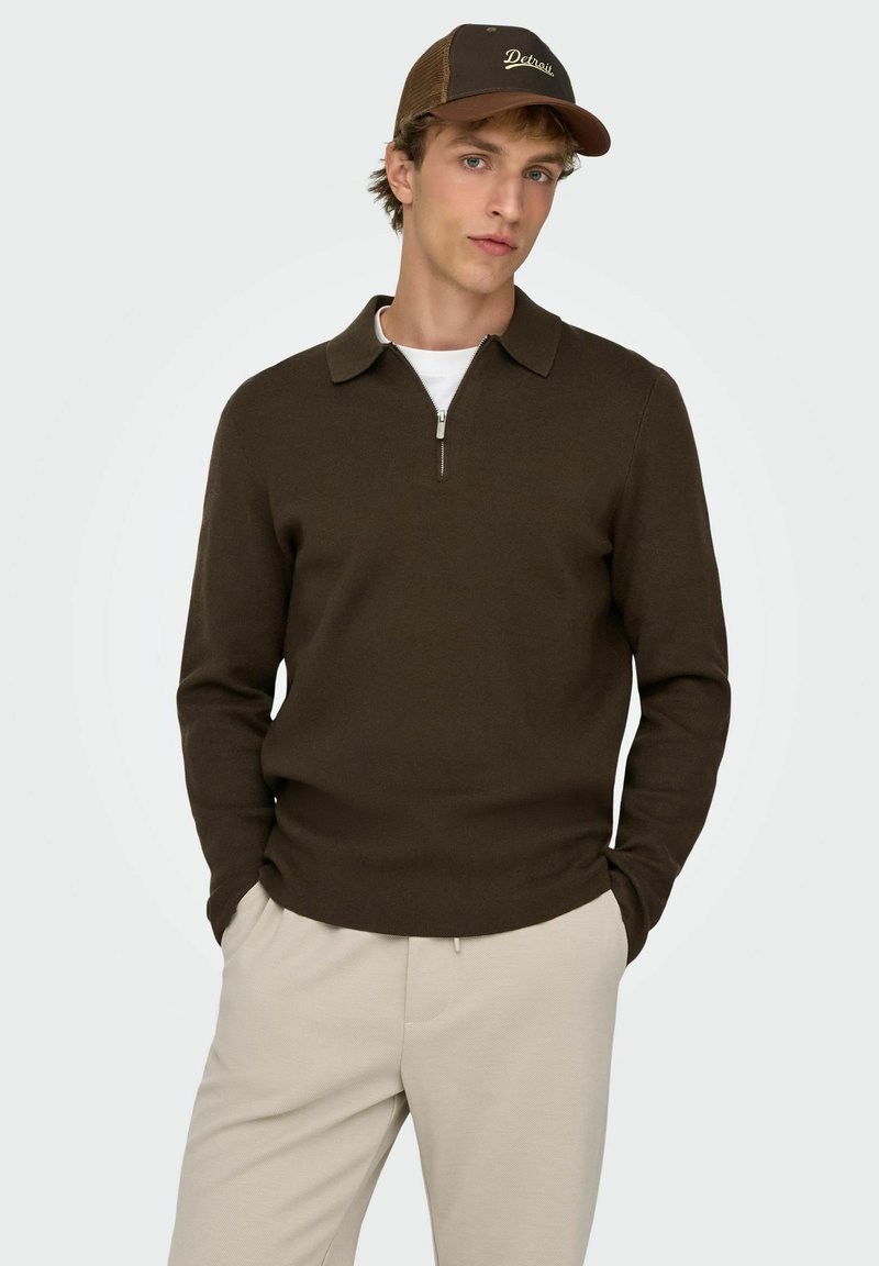 Brązowy sweter na zamek z kołnierzem, wykonany z teksturowanej tkaniny, w połączeniu z jasnobeżowymi spodniami i brązową czapką z haftem "Detroit".