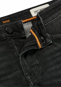 Jeans in denim nero con zip e chiusura a bottone nera, dettagli di cucitura arancione e un'etichetta con la scritta "SOFT MOTION." Texture a trama fine visibile.