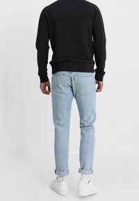 Černá mikina s dlouhými rukávy a žebrovaným lemem, doplněná o světle modré džíny s ohrnutými nohavicemi a bílé tenisky. Pohled ze zad na tuto kombinaci.