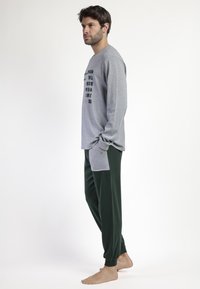 Camisa de manga larga gris con texto impreso, combinada con pantalones verde oscuro. Tela casual, corte relajado, con bolsillos laterales y puños acanalados.